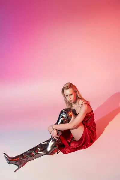 Beautiful stylish woman with long blonde hair in red dress sitting on floor on pink background — Stock Photo