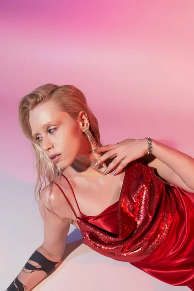 Appealing woman with accessories and tattoo in red chic dress reclining on floor on pink backdrop — Stock Photo
