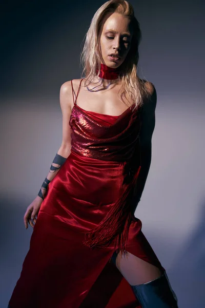 Alluring woman with long hair in red fashionable dress posing on gray backdrop and looking away — Stock Photo
