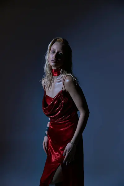 Beau modèle féminin avec des cheveux blonds en robe rouge séduisante regardant la caméra sur fond sombre — Photo de stock