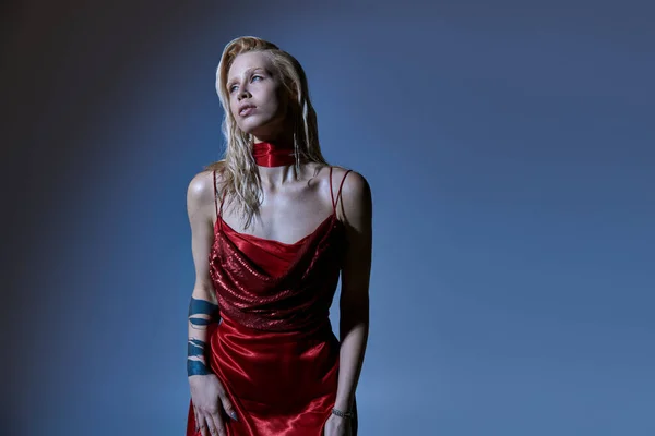 Attrayant modèle féminin élégant en robe chic rouge avec tatouage sur le bras posant sur fond sombre — Photo de stock
