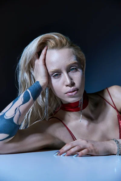 Atractiva joven modelo femenino con tatuaje y resaltador en el cuerpo posando y mirando a la cámara - foto de stock