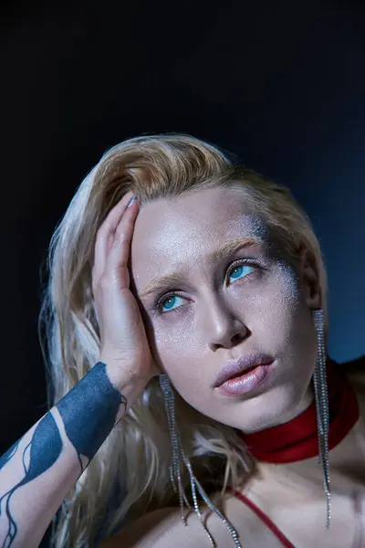 Retrato de mujer rubia de buen aspecto con accesorios y tatuaje en el brazo posando y mirando hacia otro lado - foto de stock