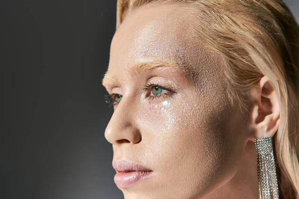 Portrait of appealing woman with earrings and green eyes posing on gray backdrop and looking away — Stock Photo