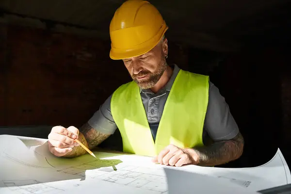 Good looking builder in safety vest and helmet working on his blueprint before construction — Stock Photo
