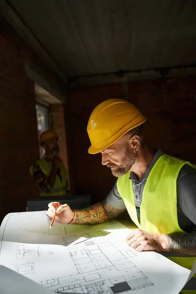 Trabajador guapo mirando plano con su colega trabajando en el telón de fondo, constructores de cabañas - foto de stock