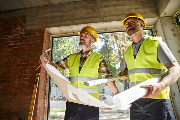 Bellissimi operai edili in caschi di sicurezza che lavorano insieme su cianografie, costruttori di case — Foto stock