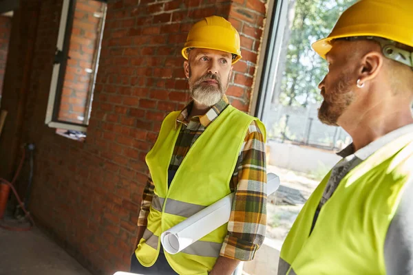 Handsome construction workers in safety helmets working together on site, cottage builders — Stock Photo