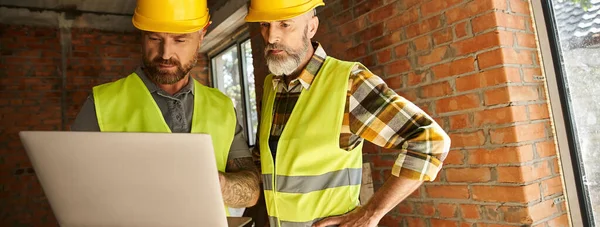 Good looking construction workers in safety vests working with laptop, cottage builders, banner — Stock Photo