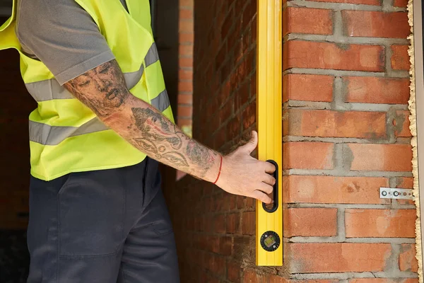 Cropped view of dedicated construction worker with tattoos using level on brick wall, builder — Stock Photo