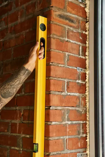 Cropped view of dedicated construction worker with tattoos using level on brick wall, builder — Stock Photo