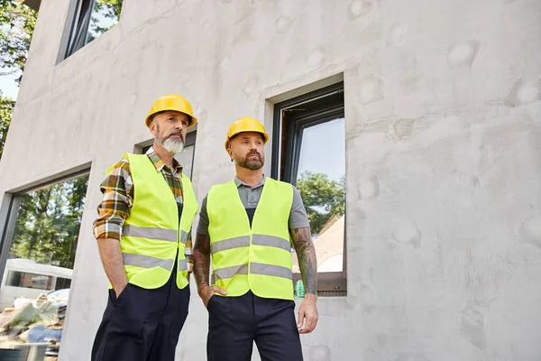 Appealing devoted builders in safety helmets and vests posing outside on construction site — Stock Photo