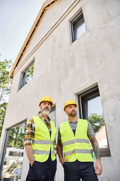 Bauarbeiter in Schutzhelmen und Westen posieren draußen auf der Baustelle — Stockfoto