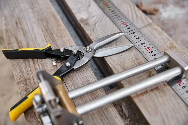 Object photo of new metal pliers lying next to measuring tape on wooden table outside of site — Stock Photo
