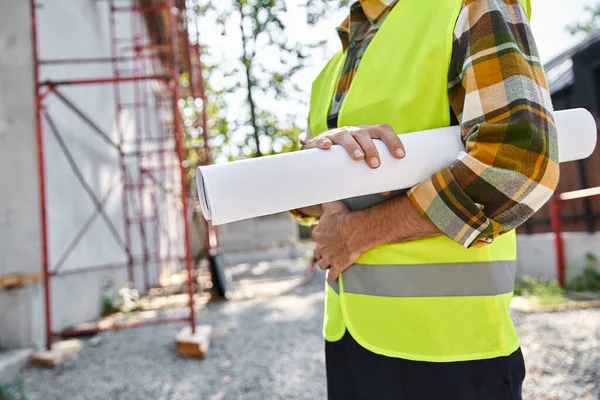 Cropped view of dedicated cottage builder with blueprint in hand posing next to scaffolding — Stock Photo