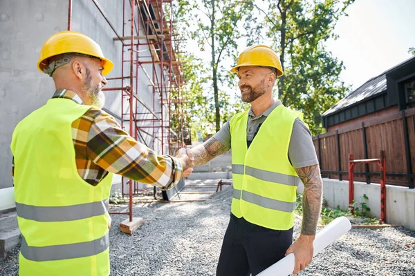 Cheerful construction workers shaking their hands and smiling at each other, cottage builders — Stock Photo
