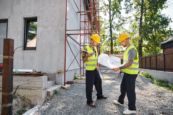 Good looking dedicated cottage builders working hard with blueprints and level on construction site — Stock Photo