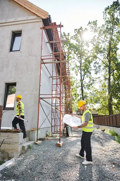 Bien parecido constructores de cabañas dedicados a trabajar duro con planos y nivel en el sitio de construcción — Stock Photo