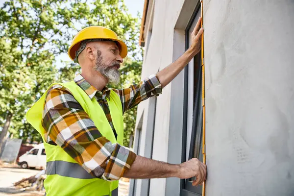 Trabajador de la construcción de buen aspecto con barba ventana de medición con cinta, constructor de casa de campo - foto de stock
