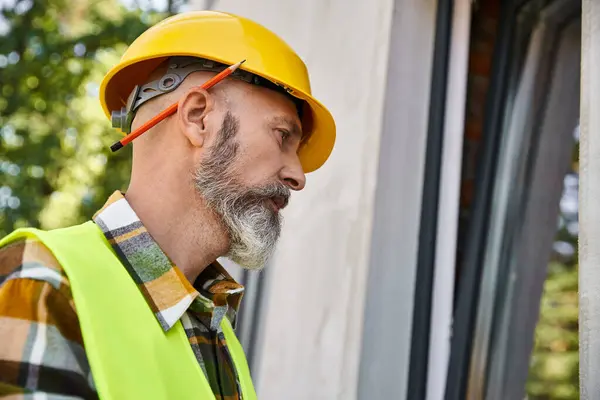 Good looking dedicated cottage builder in safety helmet looking at window while on construction site — Stock Photo