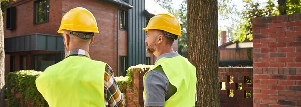 Back view of devoted construction workers in safety vests on site, cottage builders, banner — Stock Photo