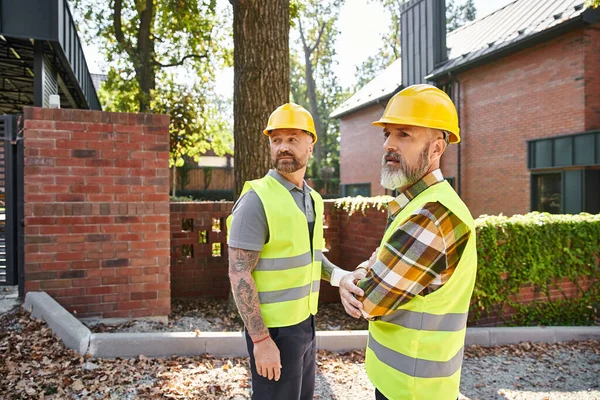 Attractive construction workers in safety helmets walking and discussing site, cottage builders — Stock Photo