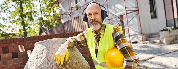 Joyeux constructeur de chalet en gants de sécurité et gilet avec écouteurs et casque souriant à la caméra, bannière — Photo de stock