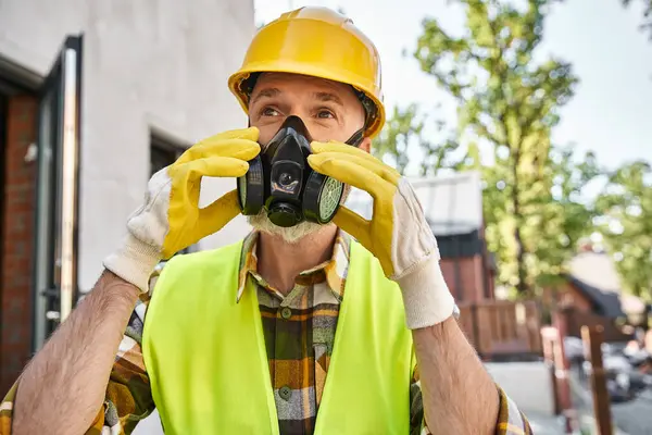 Dédié beau constructeur de chalet en gants de sécurité et masque de poussière se préparant à son travail sur le site — Photo de stock