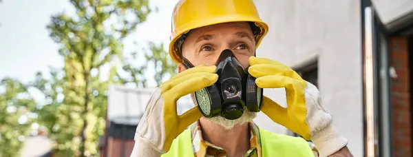 Constructor de cabaña dedicado en guantes de seguridad y máscara de polvo preparándose para su trabajo en el sitio, bandera - foto de stock