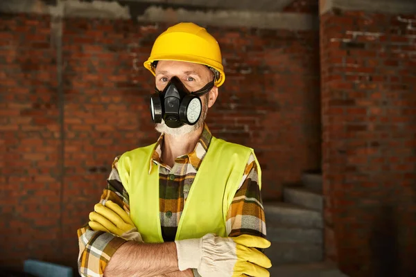 Beau constructeur de chalet avec masque de poussière dans le casque de sécurité avec les bras croisés regardant la caméra — Photo de stock