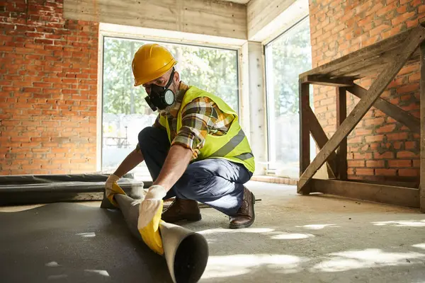 Hardworking construction worker in safety helmet and gloves with dust mask putting carpet on floor — Stock Photo