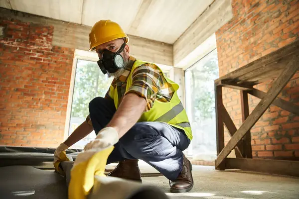 Hardworking construction worker in safety helmet and gloves with dust mask putting carpet on floor — Stock Photo