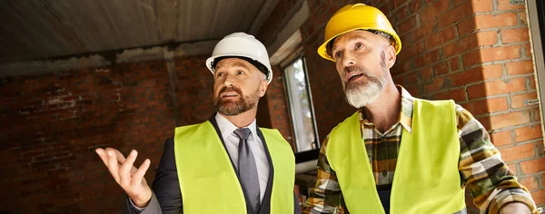 Attractive jolly cottage builder and architect discussing their work on construction site, banner — Stock Photo