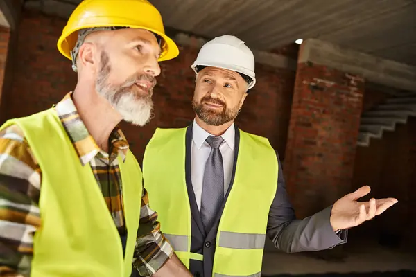 Good looking jolly cottage builder and architect discussing their work on construction site — Stock Photo