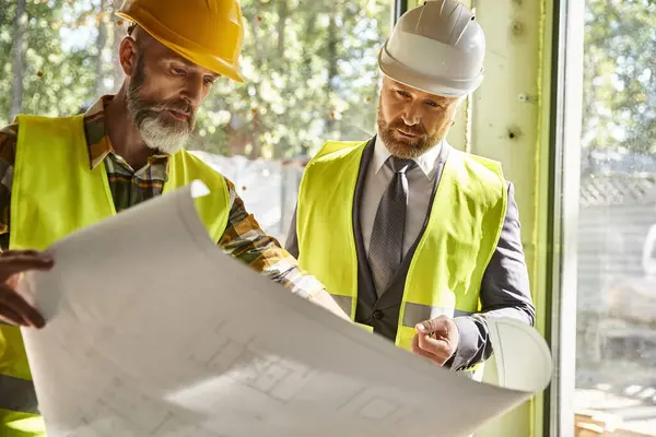 Handsome bearded businessman and cottage builder with safety gear working with blueprint on site — Stock Photo