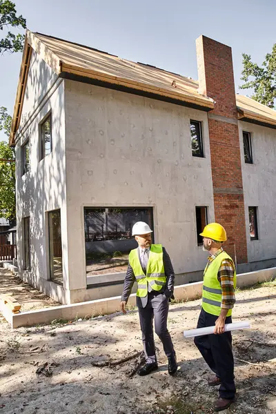 Commited architect and builder in safety vests holding blueprint and discussing construction process — Stock Photo