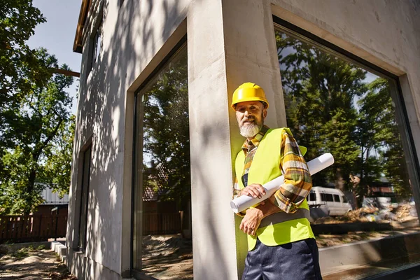 Trabajador de la construcción guapo en equipo de seguridad con el plano sonriendo a la cámara, constructor de casa - foto de stock