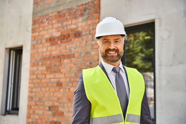 Веселий працьовитий бізнесмен у безпечному шоломі щасливо посміхається на камеру на будівельному майданчику — стокове фото