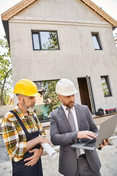 Handsome architect and builder in overalls and suit working with laptop on construction site — Stock Photo