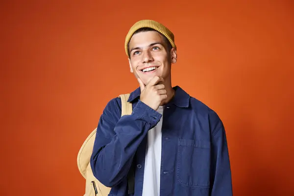 Lächelnder gutaussehender Mann mit gelbem Hut denkt über Idee vor Terrakottahintergrund nach — Stockfoto
