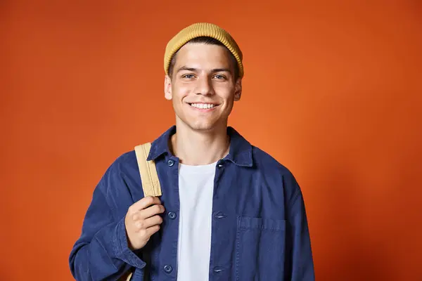 Atractivo joven en sombrero amarillo con ojos grises sonriendo a la cámara sobre fondo de terracota - foto de stock