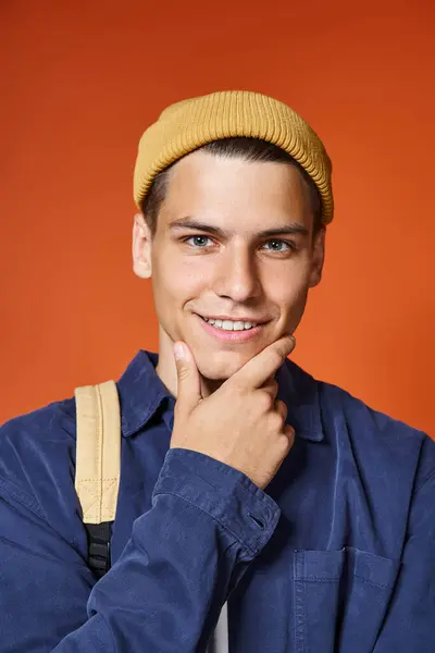 Portrait of charming young man in yellow hat with grey eyes touching to chin with hand — Stock Photo