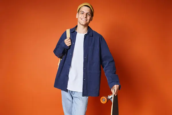 Charismatic young man in casual outfit standing with skateboard against terracotta background — Stock Photo