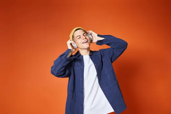 Attractive young guy pleasure listening to music with headphones on terracotta background — Stock Photo