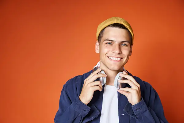 Schöner junger Mann mit Kopfhörern und gelbem Hut, der auf Terrakottahintergrund in die Kamera lächelt — Stockfoto