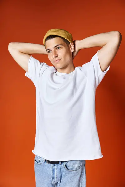 Charming young guy in white t-shirt and yellow hat standing putting hands behind back — Stock Photo