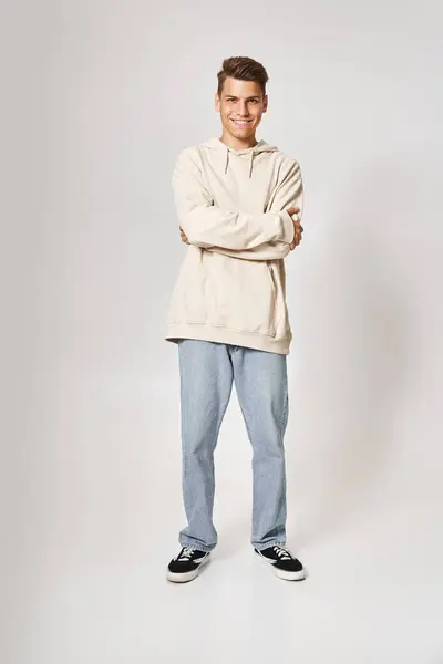 Handsome young man in white hoodie smiling with folded arms against light background — Stock Photo