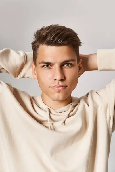 Confident young man in white hoodie putting hands behind head against light background — Stock Photo