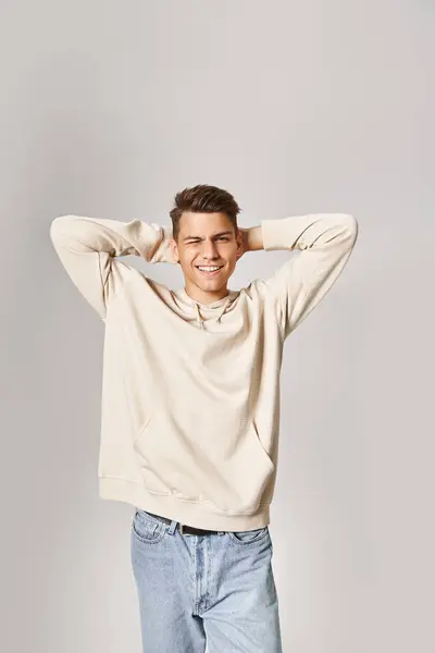 Charming guy in white hoodie putting hands behind head and winking to camera on light background — Stock Photo