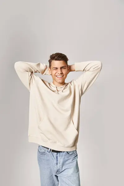 Charming guy in white hoodie putting hands behind head and winking to camera on light background — Stock Photo